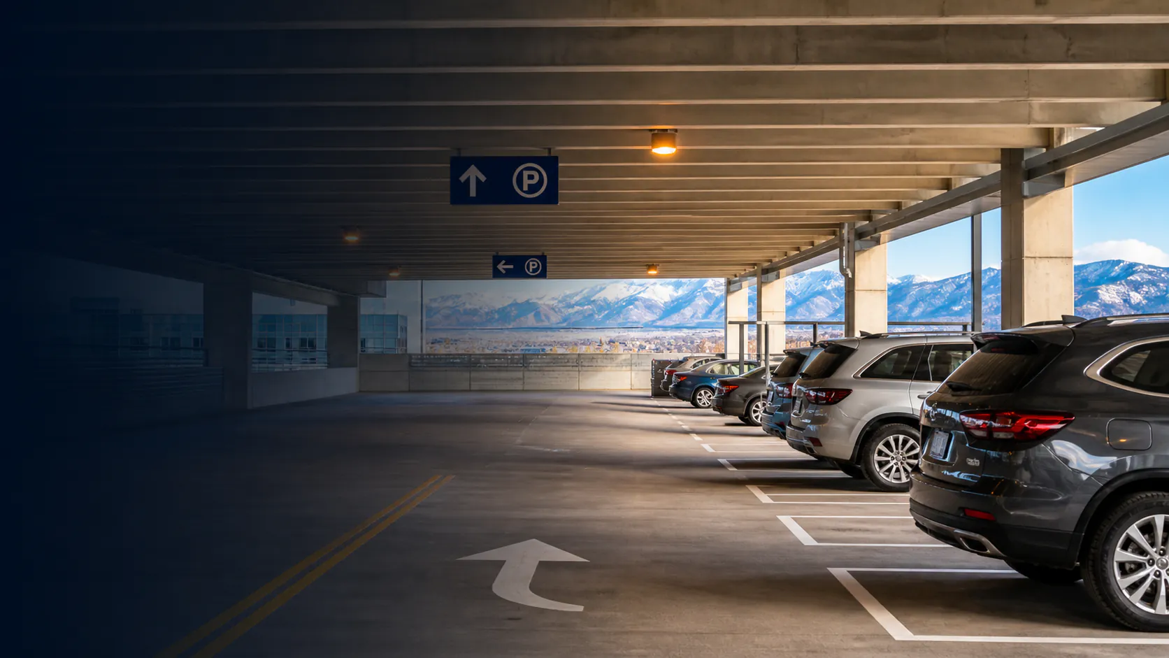 A clean multi-level Utah parking garage with orderly vehicles, clear lanes, warm lighting, and the snow-covered Wasatch Mountains beyond.